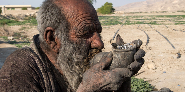 Amou Haji (uncle Haji) smokes from his waterpipe as he sits on the ground on the outskirts of the village of Dezhgah in the Dehram district of the southwestern Iranian Fars province, on December 28, 2018. - Believed to be the worlds dirtiest man, villagers say that Haji's leather-like skin hasn't touched soap and water for more than sixty years. They believe that he decided to live in isolation after suffering from an emotional setback in his youth. (Photo by - / AFP) (Photo by -/AFP via Getty Images)