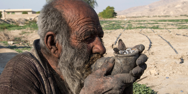 Amou Haji (uncle Haji) smokes from his waterpipe as he sits on the ground on the outskirts of the village of Dezhgah in the Dehram district of the southwestern Iranian Fars province, on December 28, 2018. - Believed to be the worlds dirtiest man, villagers say that Haji's leather-like skin hasn't touched soap and water for more than sixty years. They believe that he decided to live in isolation after suffering from an emotional setback in his youth. (Photo by - / AFP) (Photo by -/AFP via Getty Images)