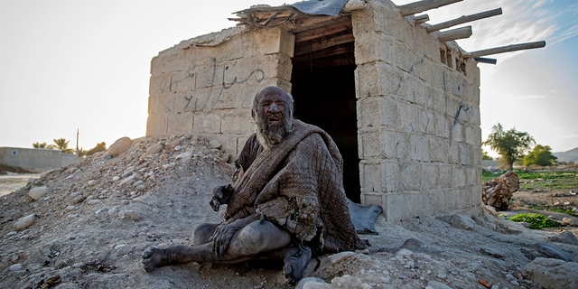 Amou Haji sits in front of an open brick shack that villagers constructed for him on the outskirts of Dezhgah, Iran, on Dec. 28, 2018.