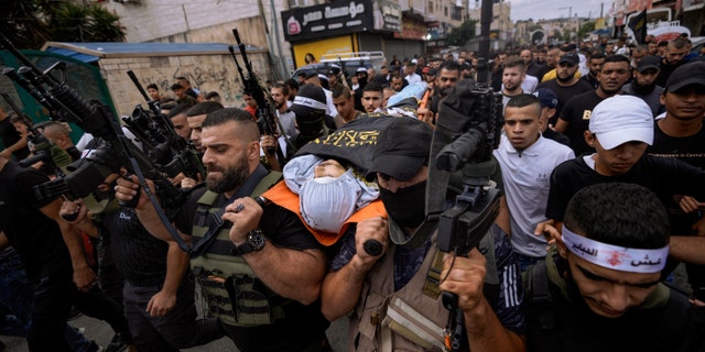 Armed Palestinians carry the body of Mahmoud al-Sus, covered in the flag of the Islamic Jihad group, during his funeral in the West Bank town of Jenin on Saturday, October 8, 2022. A shootout during a military raid in the West Bank.  (AP Photo/Majidi Mohammed)