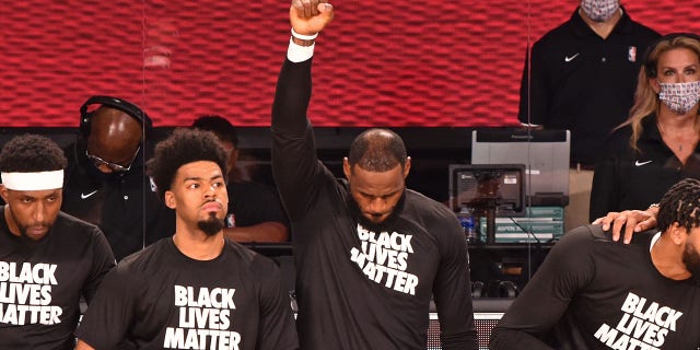 LeBron James of the Los Angeles Lakers raises his fist while kneeling for the national anthem before a game against the LA Clippers July 30, 2020, in Orlando, Fla.