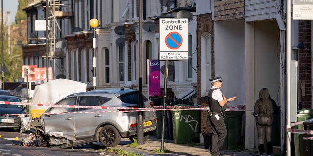 A police officer speaks to local residents the morning after two men were killed in a double shooting on the Railton Road between Herne Hill and Brixton in London October 31, 2022. Debris was scattered across the street after Met Police were called around 19:50 GMT the night before after witnesses heard reports of gunfire between a car and a moped.