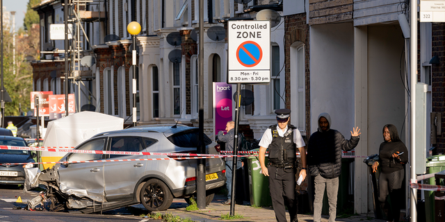 A police officer speaks with local residents the morning after two males were killed in a double-shooting on Railton Road, between Herne Hill and Brixton, on Oct. 31 2022, in London. Wreckage has been spread across the road after Met police were called at about 7:50 p.m. GMT the night before, after reports of gunshots between a car and moped were heard by witnesses.