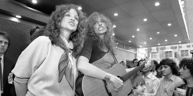 FILE - Lucy Simon, left, and her sister Carly Simon sing in Broadway's Shubert Alley in New York, on June 9, 1982. 