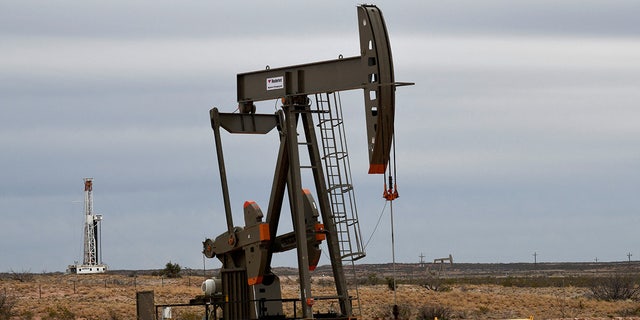 A pump jack operates in front of a drilling rig near Carlsbad, New Mexico.
