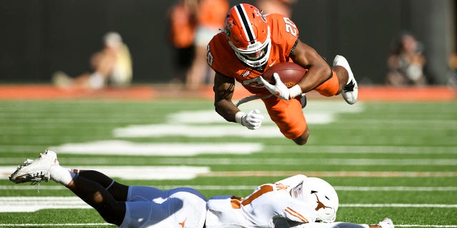 Oklahoma State running back Dominic Richardson (20) launches himself over Texas defensive back Anthony Cook, bottom, during the first half of an NCAA college football game Saturday, Oct. 22, 2022, in Stillwater, Okla.