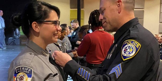 El sargento de policía de Escondido.  Jeff Valdivia coloca la insignia en el uniforme de la diputada del condado de El Paso, Natalie Young, luego de su ceremonia de graduación.