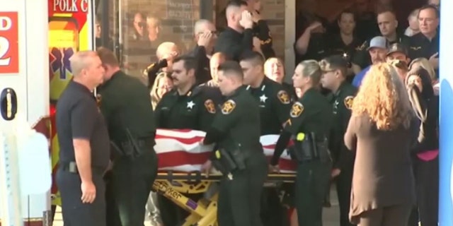 Deputies salute the flag-draped body of a fallen deputy as they place him into an ambulance.