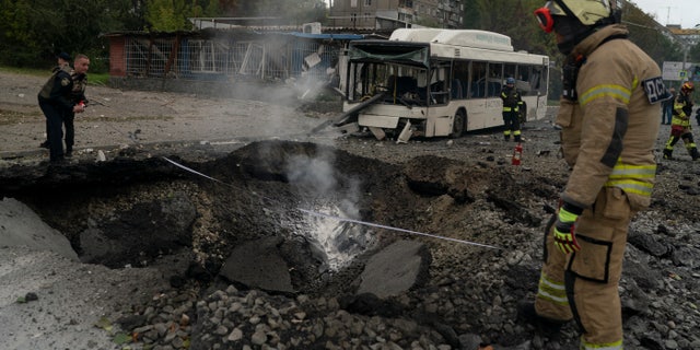 Firefighters and police officers work at the site where an explosion created a crater in the street after a Russian attack in Dnipro, Ukraine, Monday, October 10, 2022.  (AP Photo/Leo Correa)