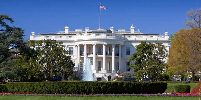 The White House lawns are beautifully landscaped lawns with flowers, fountains and blooming trees is in foreground.