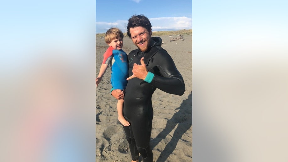 Michael Trainor, wearing a wetsuit, poses for a photo with his son