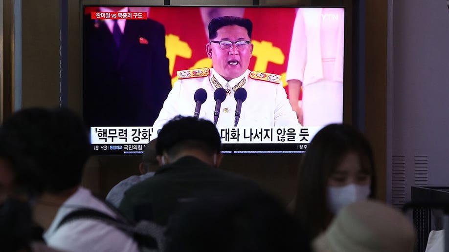 Kim Jong Un is seen on a TV screen wearing an all white military uniform