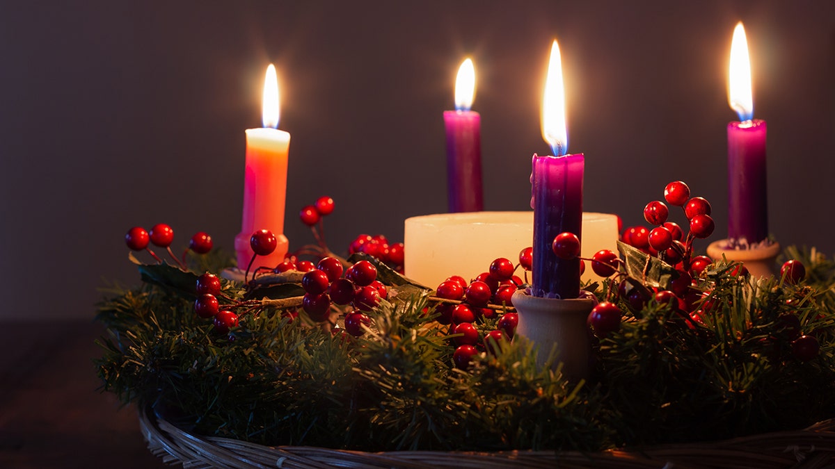 Four lit advent candles in a dark room