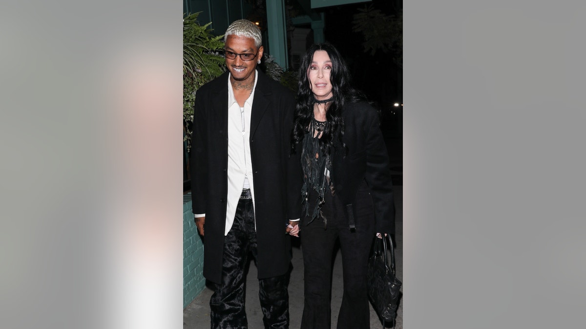 Cher in all black and her boyfriend Alexander Edwards in a white shirt and black jacket