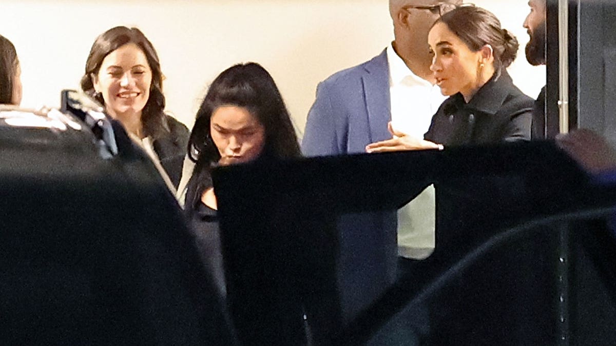 Meghan Markle gestures to someone as she gets into the car outside the hotel