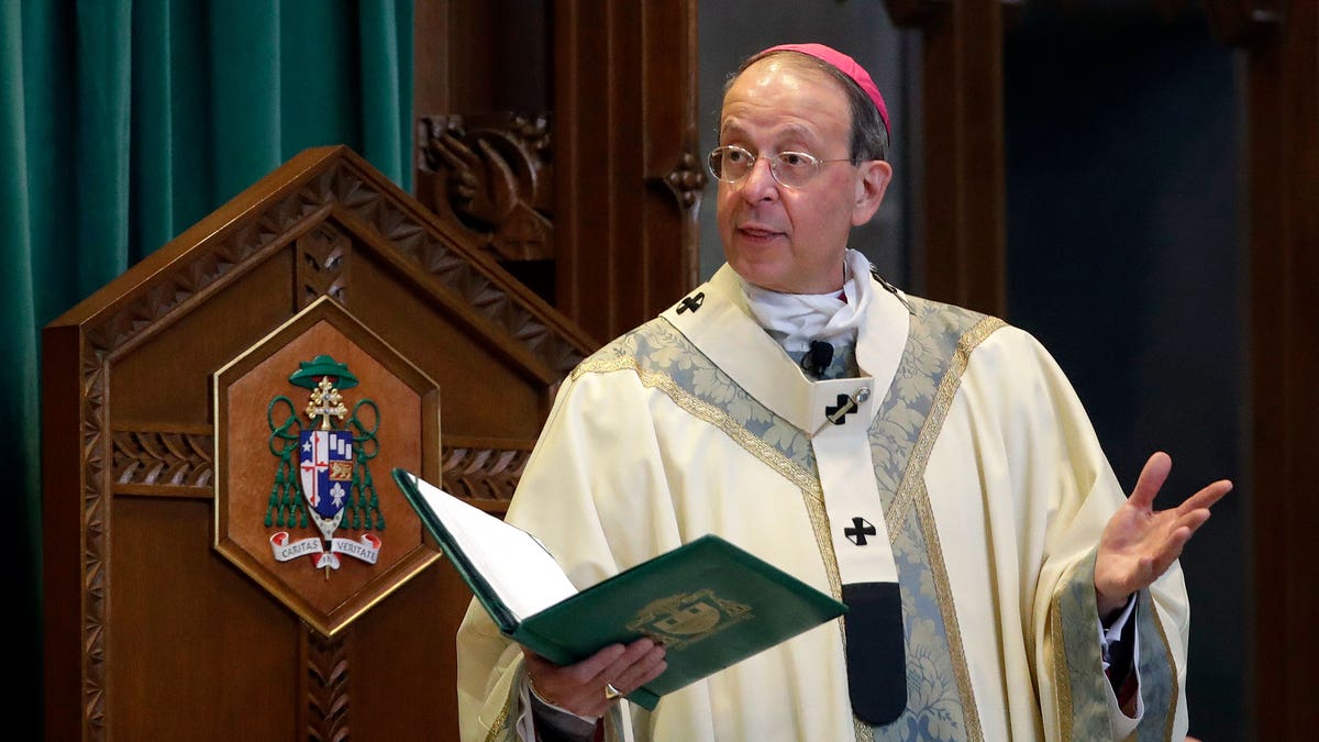 Catholic Archbishop preaching from the pulpit and holding a green book.