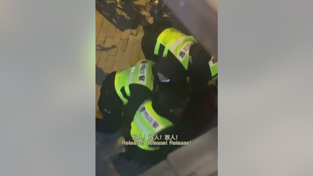 Three Chinese officers in reflective vests detaining a BBC reporter