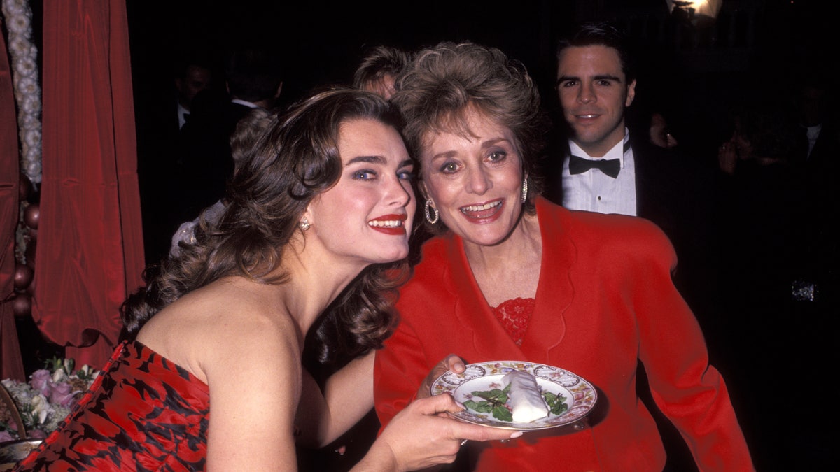 Brooke Shields in a red dress smiles and holds a plate with Barbara Walters in a red suit at the Plaza Hotel in 1991