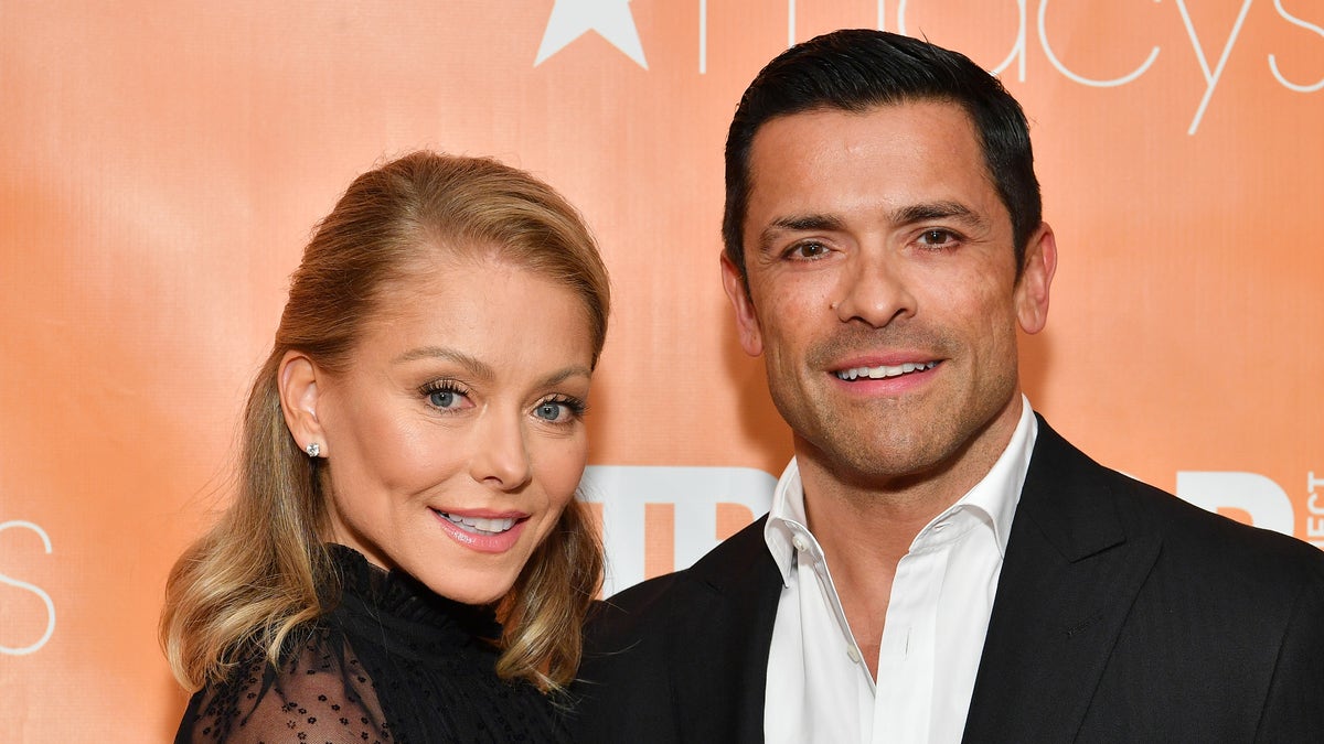 Kelly Ripa smiles in a black dress next to her husband Mark Consuelos in a white button down and black suit