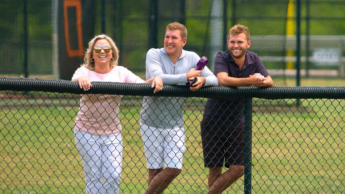 Julie, Todd and Chase Chrisley stand behind a black fence during a scene from "Chrisley Knows Best"