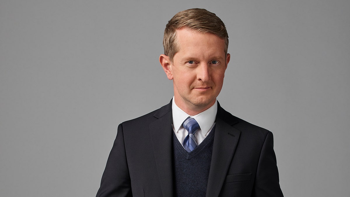 Ken Jennings in a black suit and blue tie poses for a picture