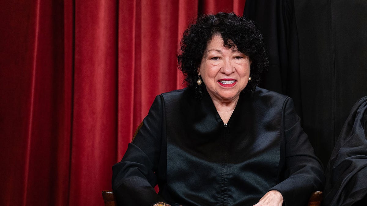 Justice Sotomayor successful  judicial robes with reddish  curtain down  her