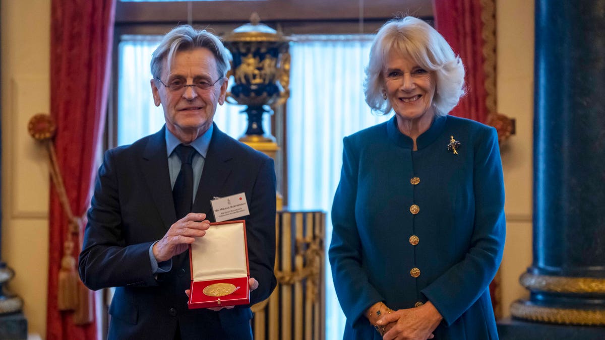 The Queen Consort smiles next to Mikhail Baryshnikov who holds his medal in a red box