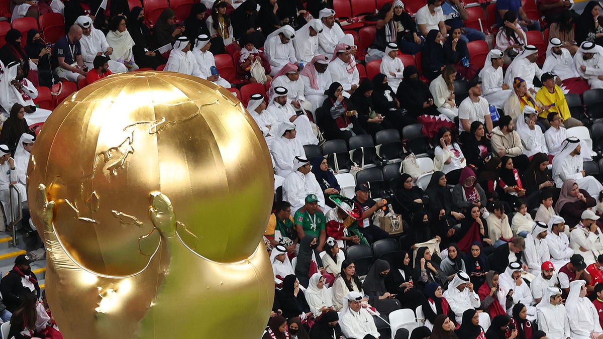 Fans are seen in the background of a replica of the FIFA World Cup trophy