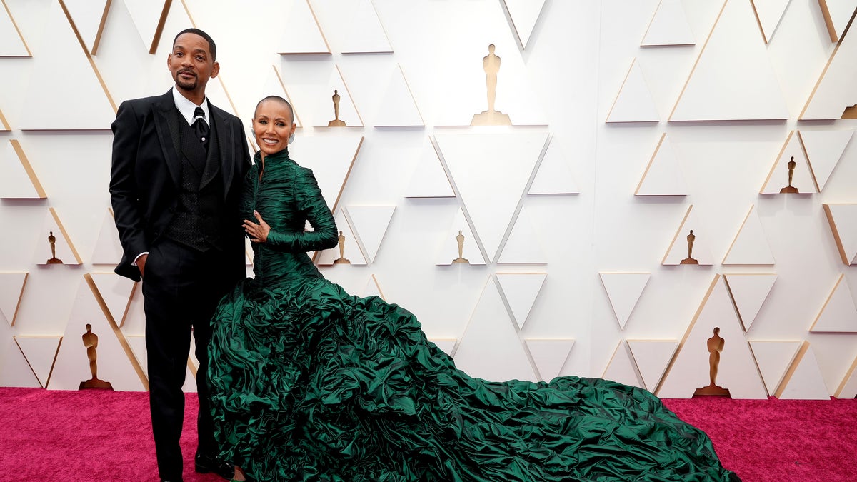Will Smith stands next to his wife Jada in a long green gown with a feathered train at the 2022 Oscars