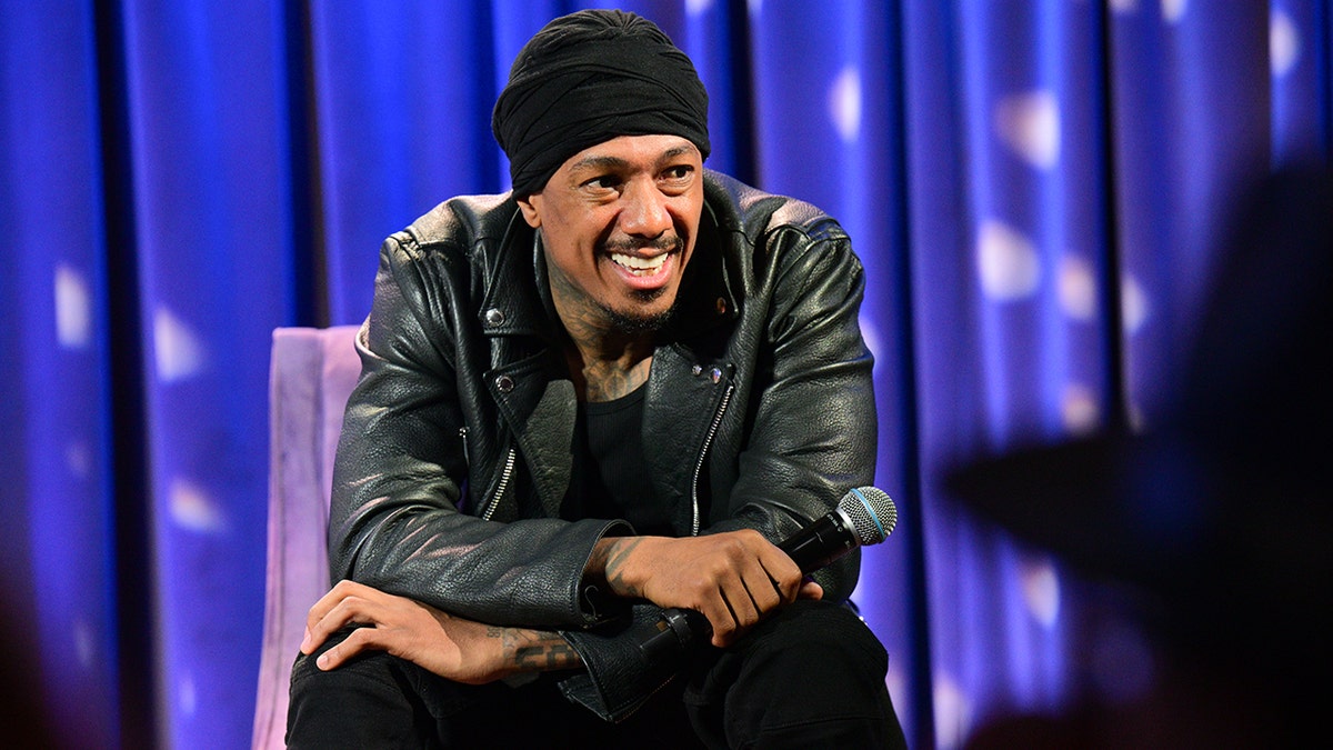 Nick Cannon smiles to the right in an all-black outfit