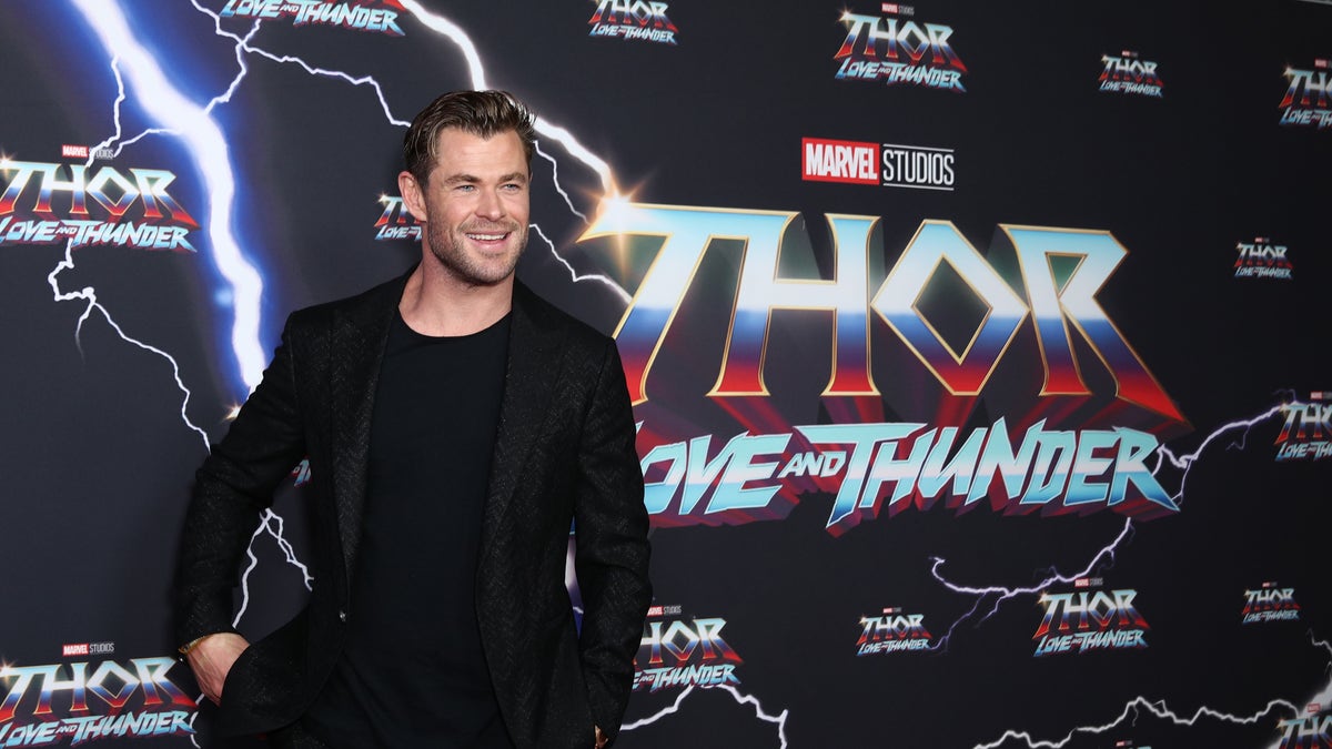 Chris Hemsworth smiles on the red carpet in an all black outfit for the "Thor: Love And Thunder" premiere in Australia