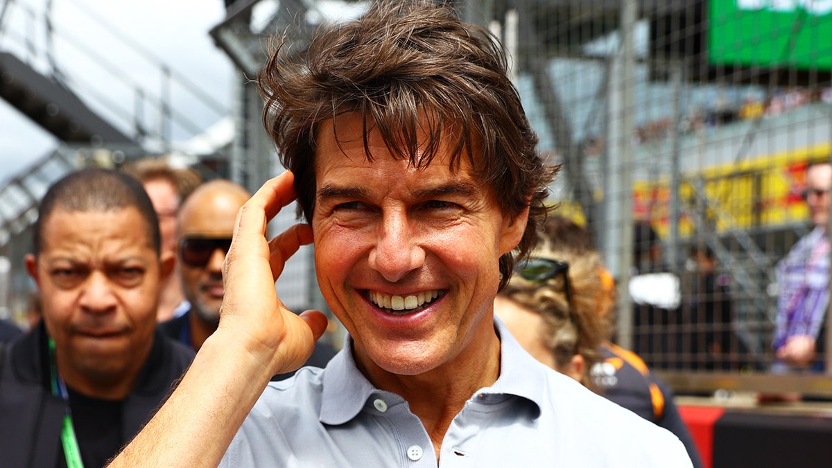 Tom Cruise looks as though he's about to push back his hair as he smiles in a crowd of fans in England
