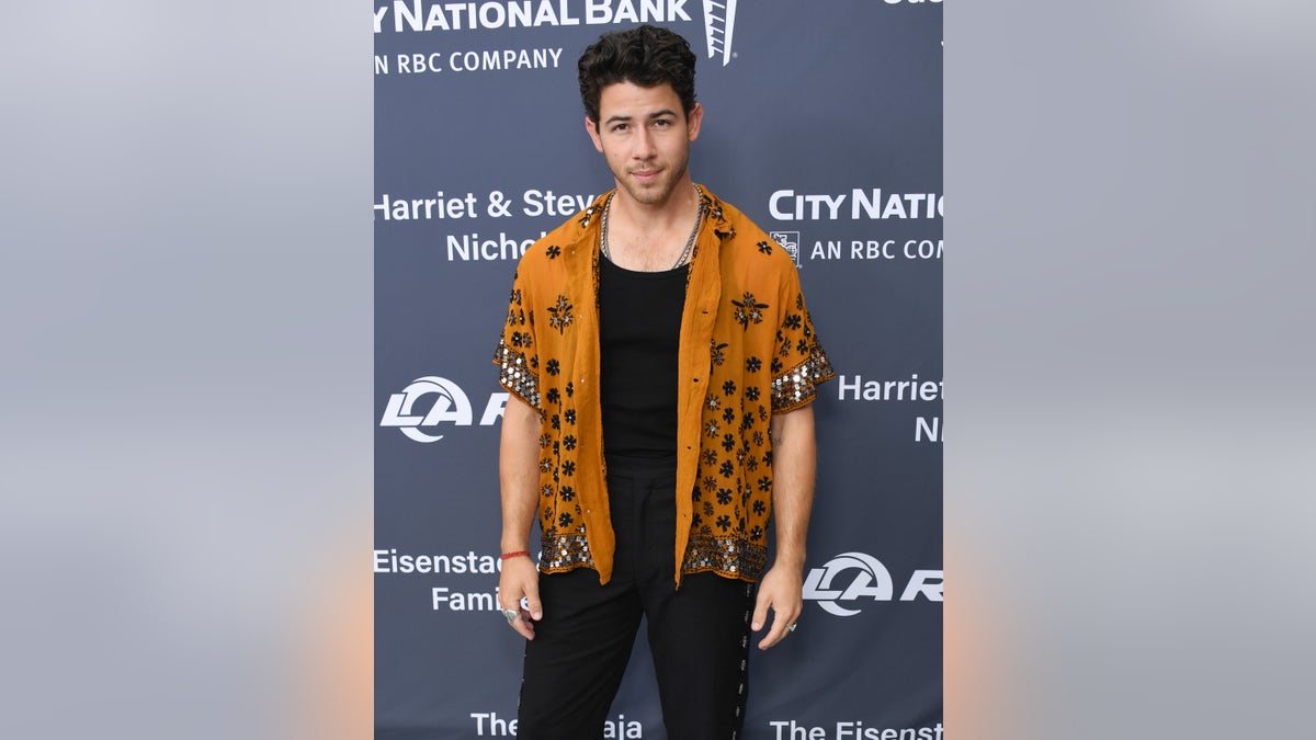 Nick Jonas with a black undershirt and on orange-sequined button up short-sleeve shirt