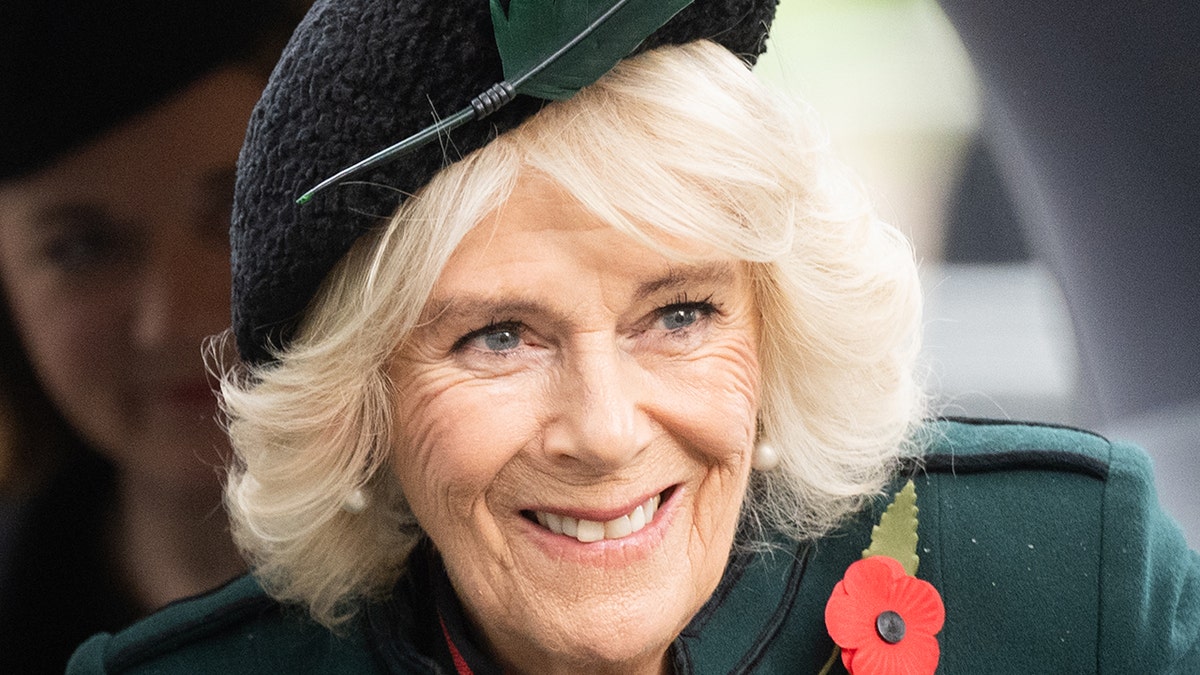Camilla Parker Bowles, the Queen Consort smiles in a green jacket and matching hat