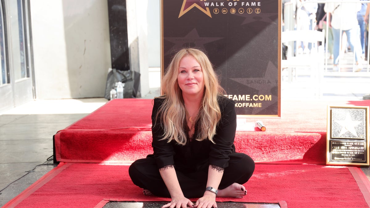 Christina Applegate sits on the ground at her star on the Hollywood Walk of Fame induction in a black suit