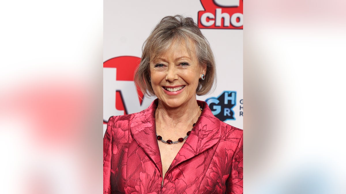 Jenny Agutter smiles in a red suit outlined with flowers on the red carpet