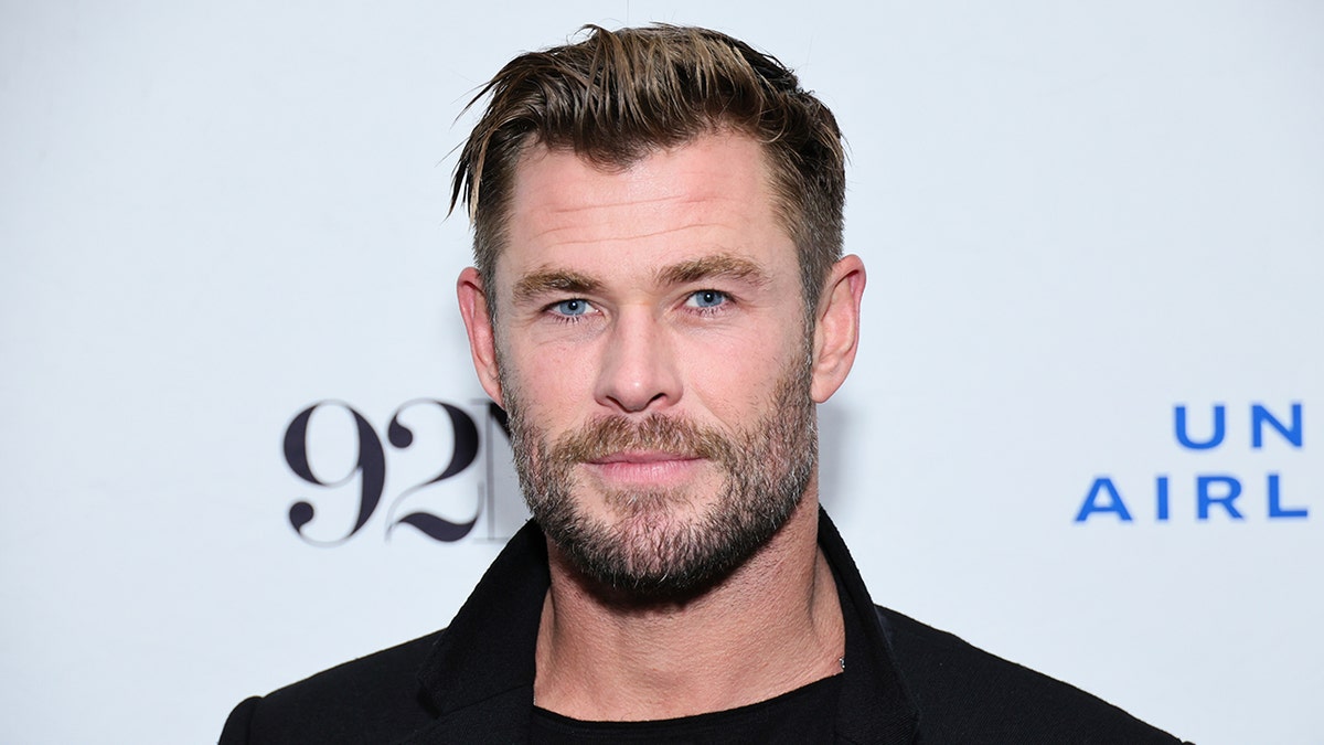 Chris Hemsworth smiles for a photo on the red carpet in a black outfit