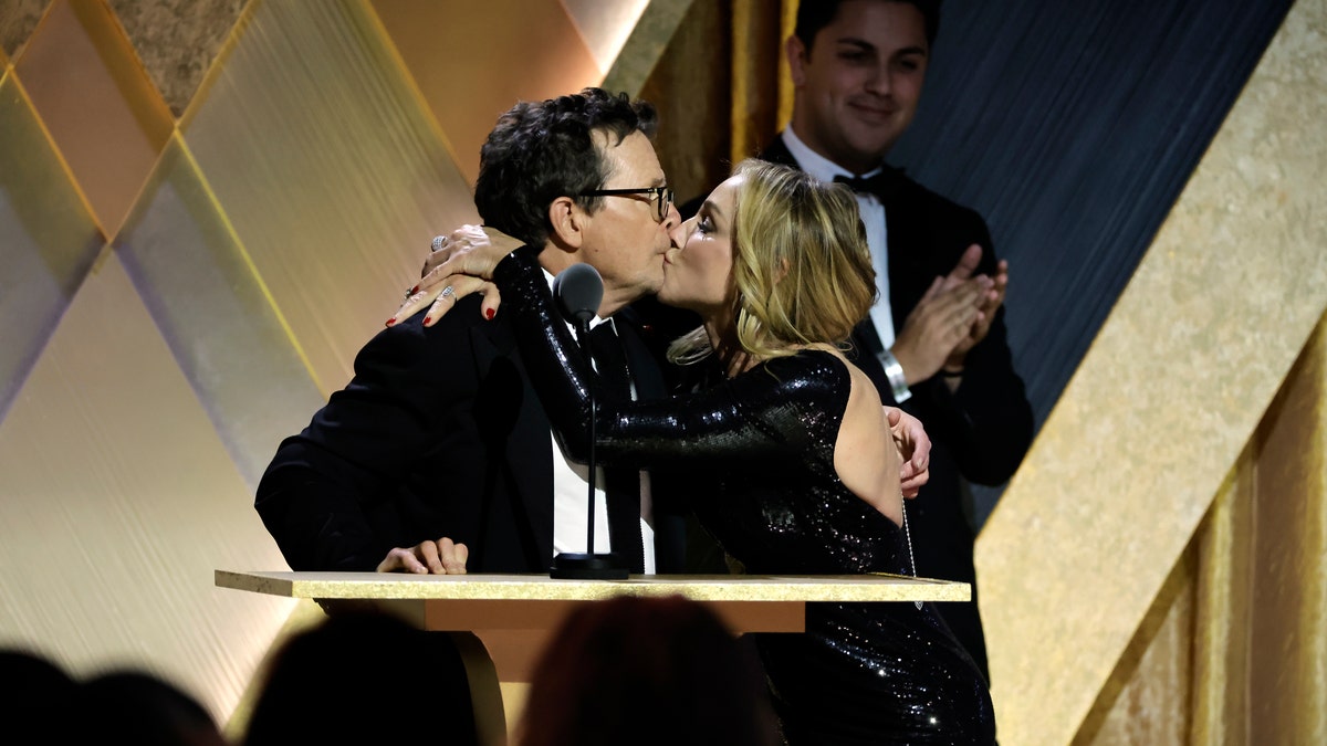Tracy Pollan wraps her arms around husband Michael J. Fox and gives him a kiss on stage