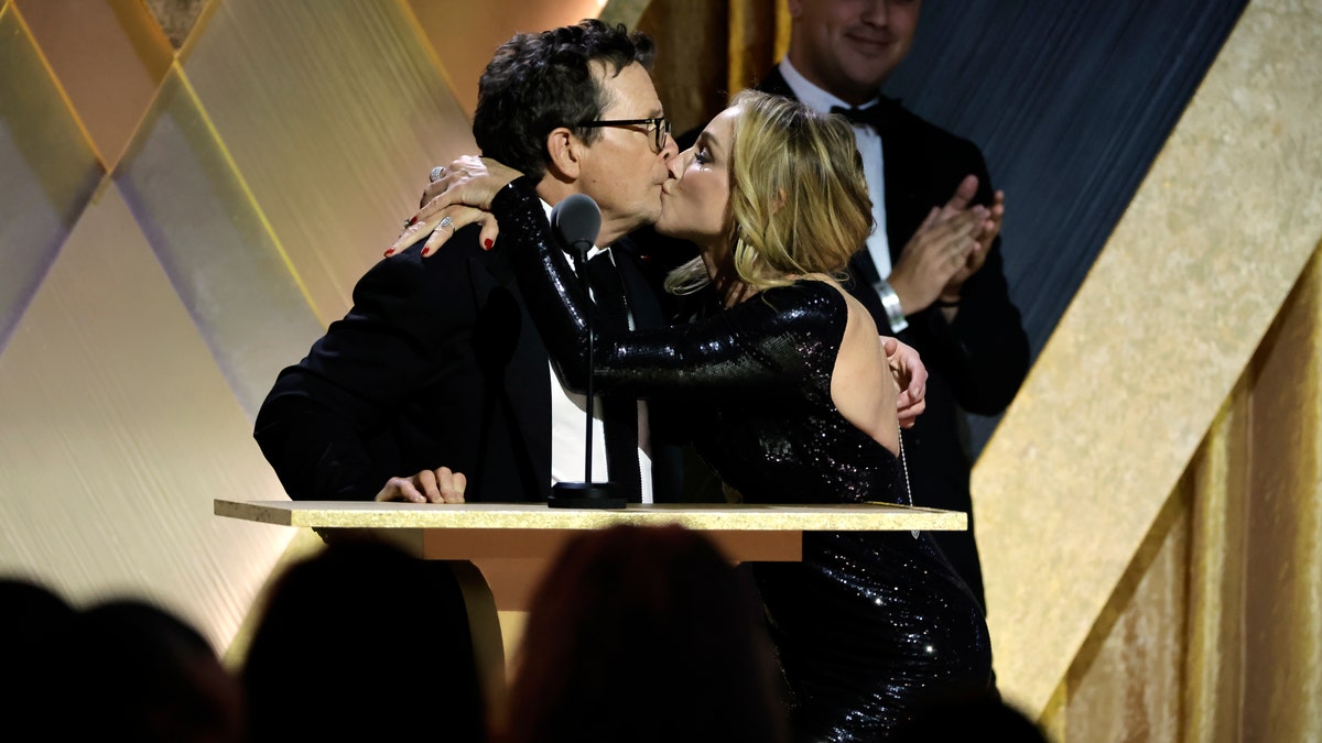 Tracy Pollan wraps her arms around husband Michael J. Fox and gives him a kiss on stage