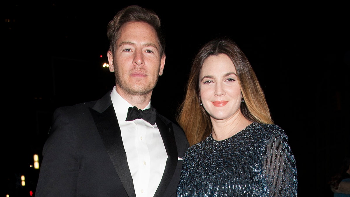 Will Kopelman in a black tuxedo poses with wife Drew Barrymore in a dark dress in New York