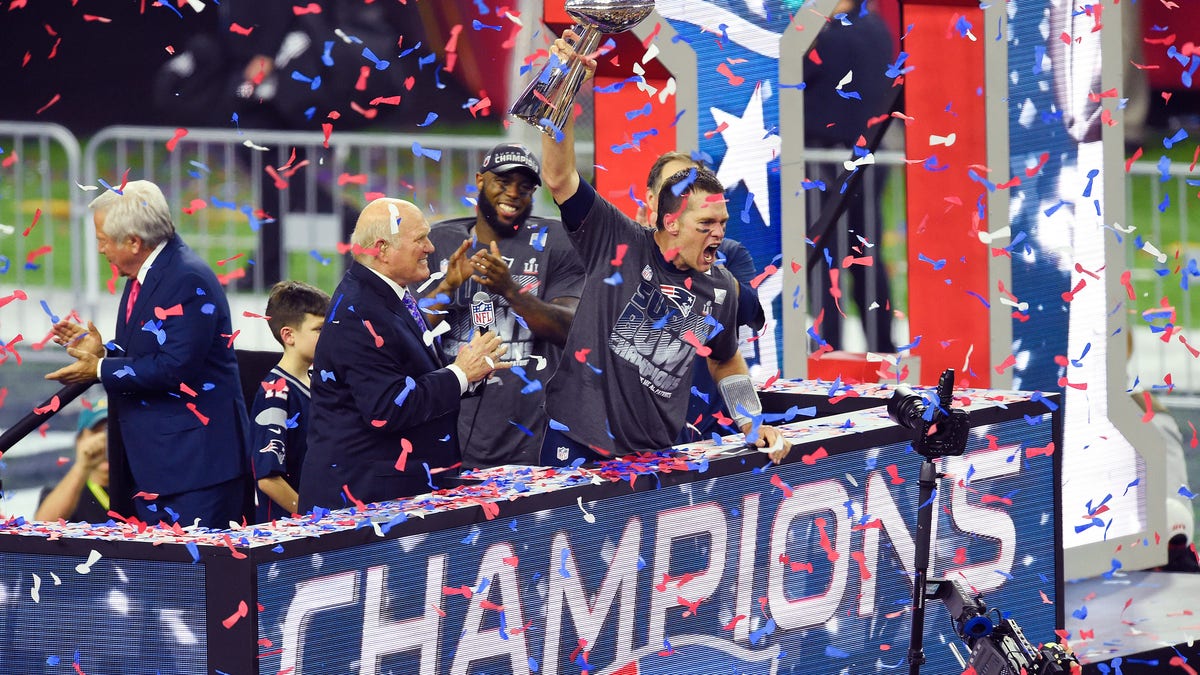 Tom Brady celebra la victoria de los New England Patriots en el Super Bowl 2017 con confeti cayendo del cielo mientras iza el Trofeo Lombardi.