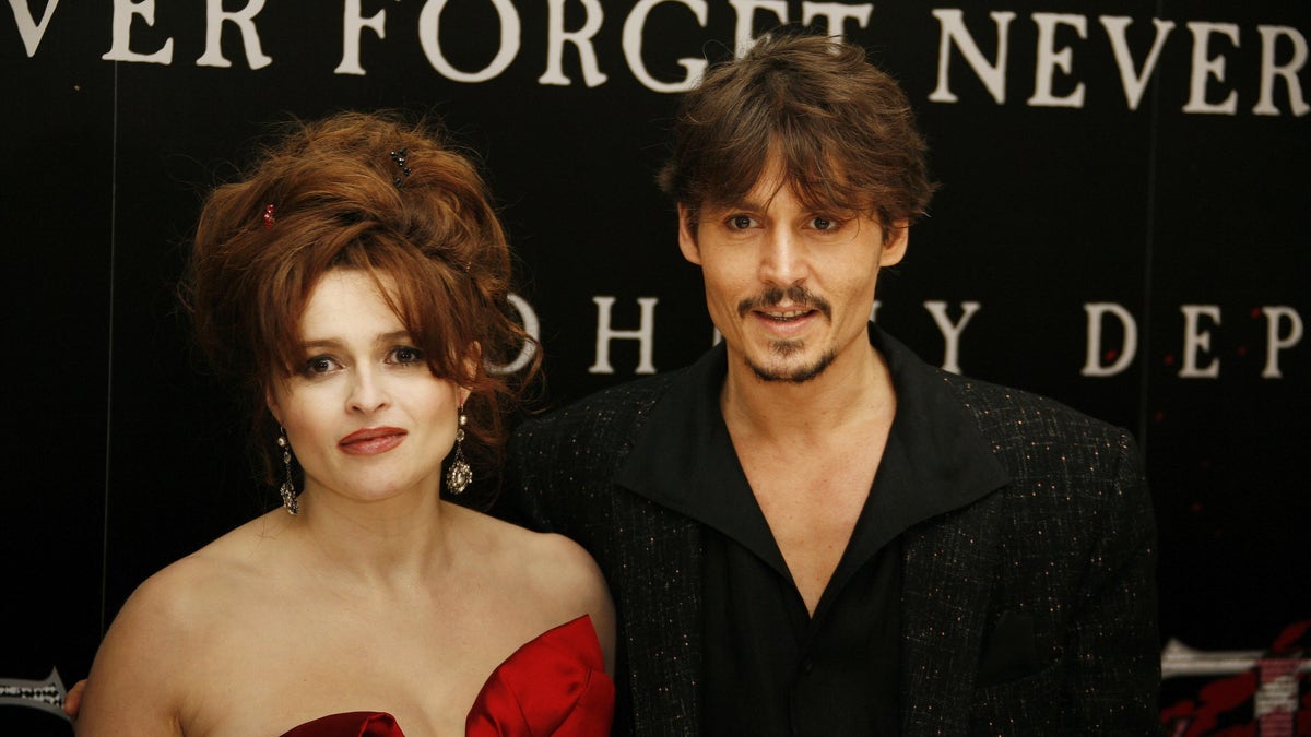 Helena Bonham Carter ina red strapless dress poses with Johnny Depp in an all black outfit on the red carpet