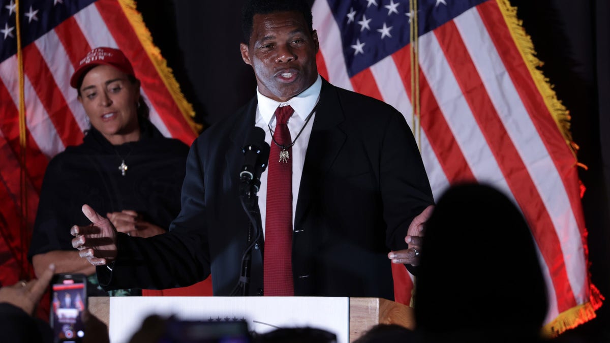 Geoergia Senate candidate Herschel Walker seaking with girl wearing red hat behind him