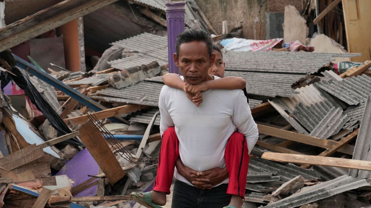 Man carries is child on his back while they walk through the debris.