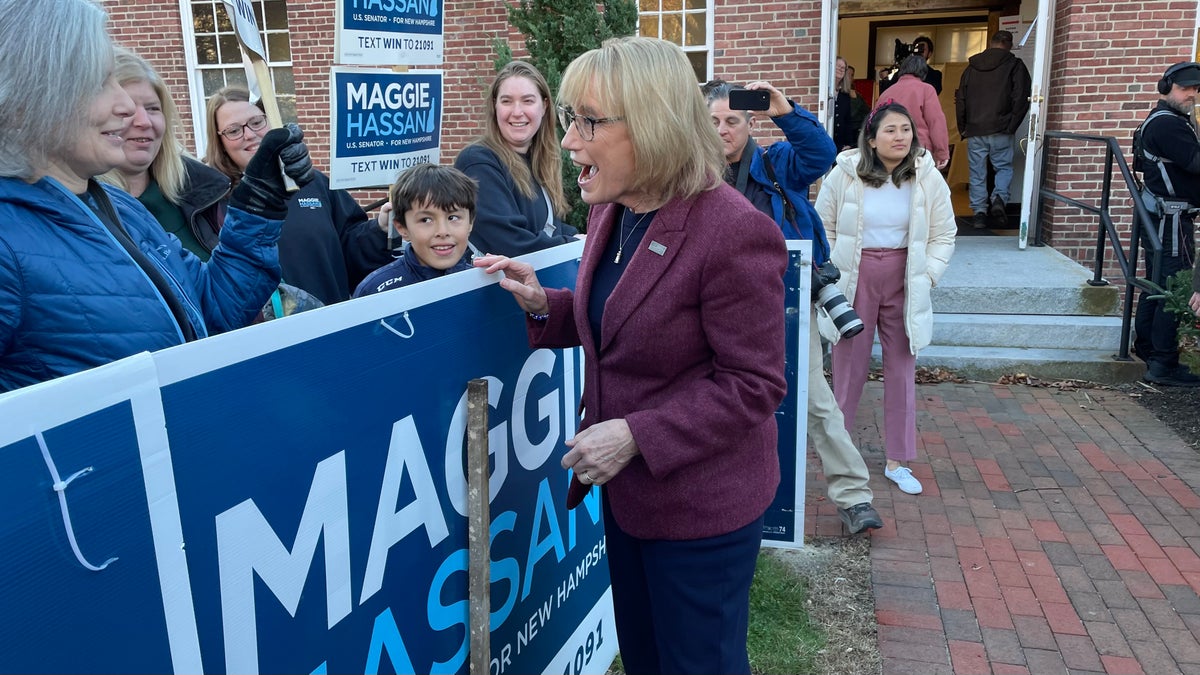 Maggie Hassan stands in front of a campaign sign while talking to canvassers