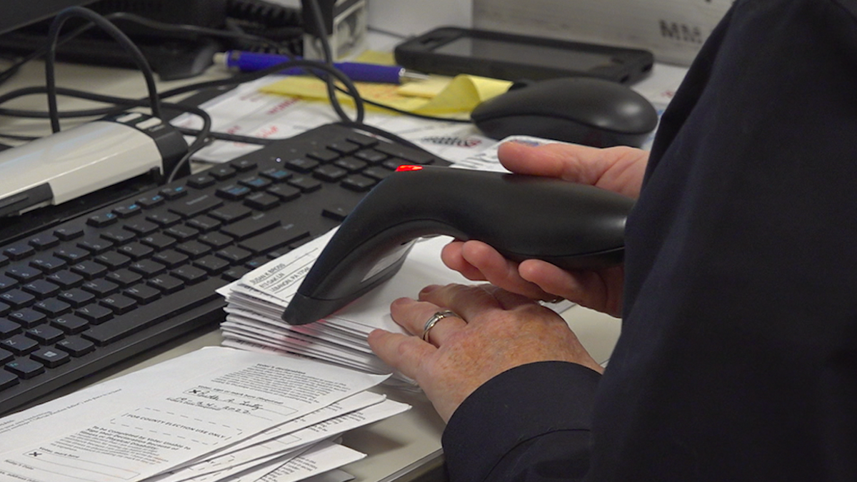 Woman holding a scanner processing a pile of mail-in ballots