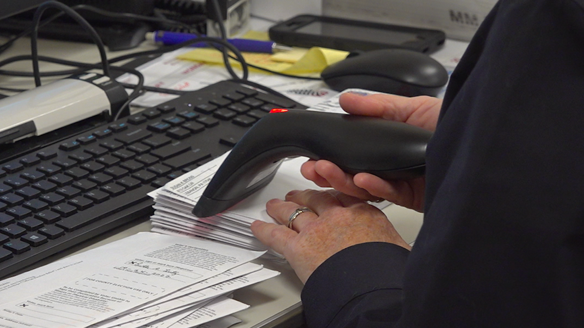 Woman holding a scanner processing a pile of mail-in ballots