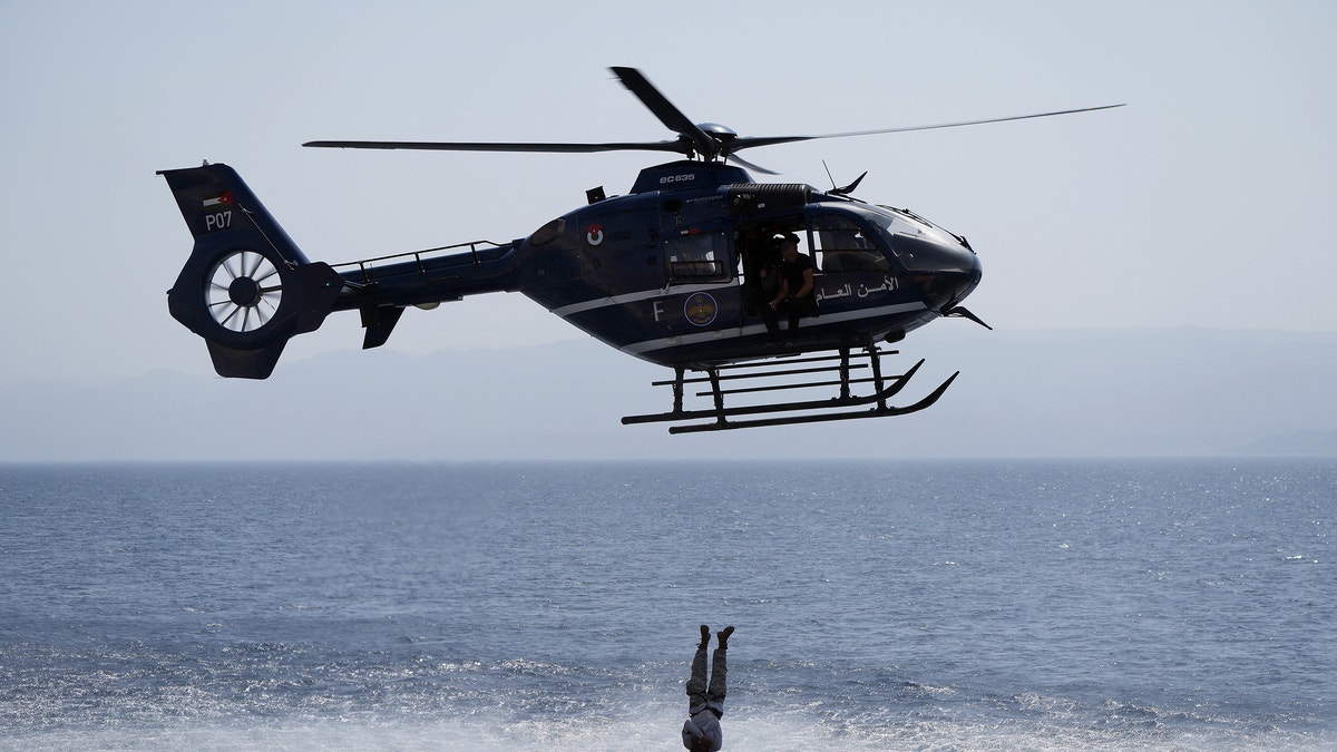 A helicopter hovers of water while a contestant dives into the ocean
