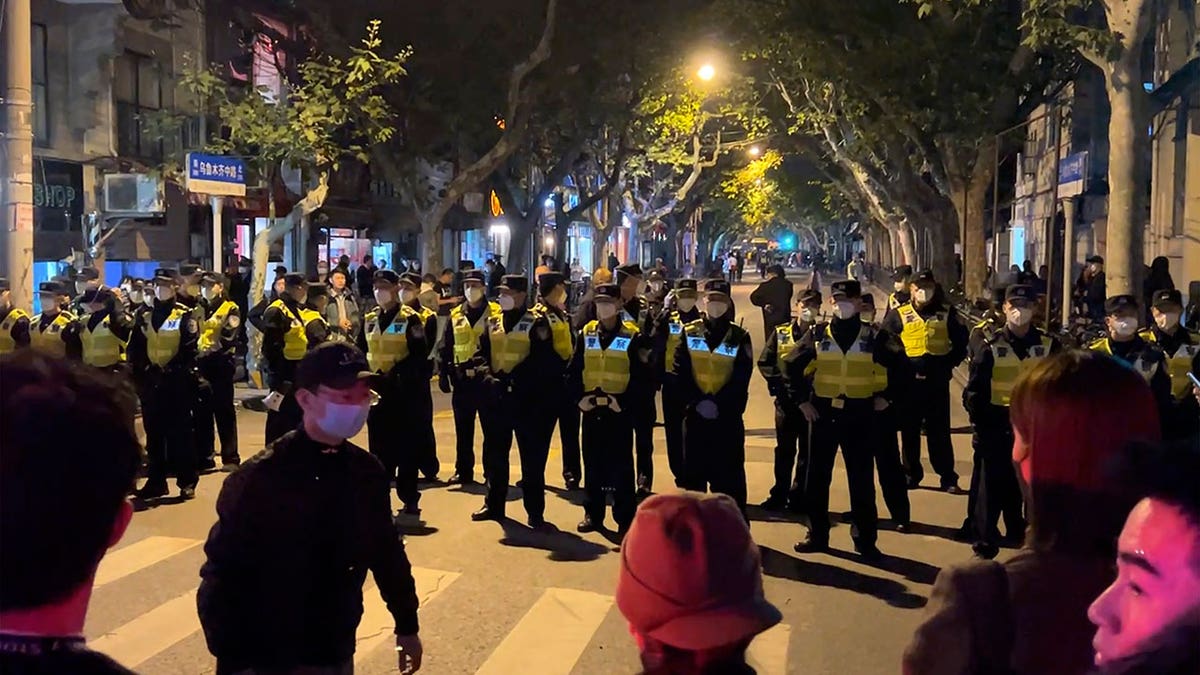 Chinese police stand in a line on front of covid protestors