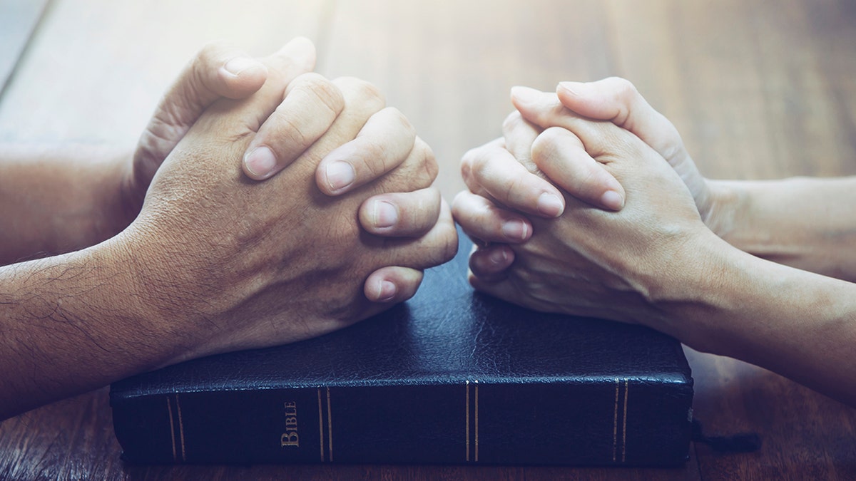 Couple praying with hands on bible